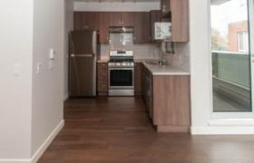 Bright kitchen with hardwood floors, stainless steel appliances, and a city view through sliding glass doors.