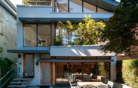 Modern patio with outdoor dining set, large glass windows, and lush greenery.