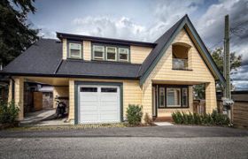 Exterior of a laneway house with yellow brick siding, a white garage door, and a dark shingled roof.