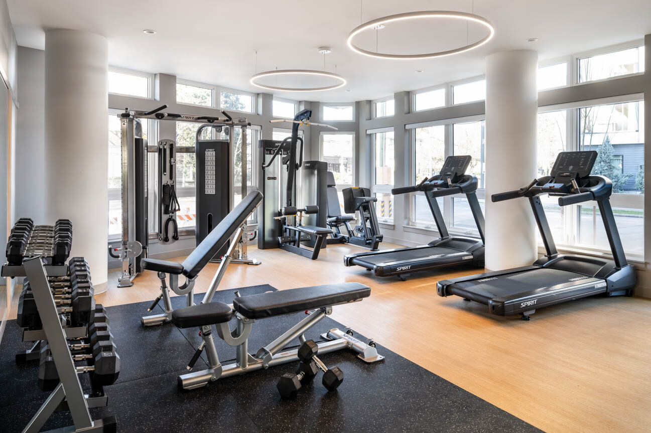 Fitness room featuring Spirit treadmills, weight benches, and large windows with circular pendant lights. - City Oxford