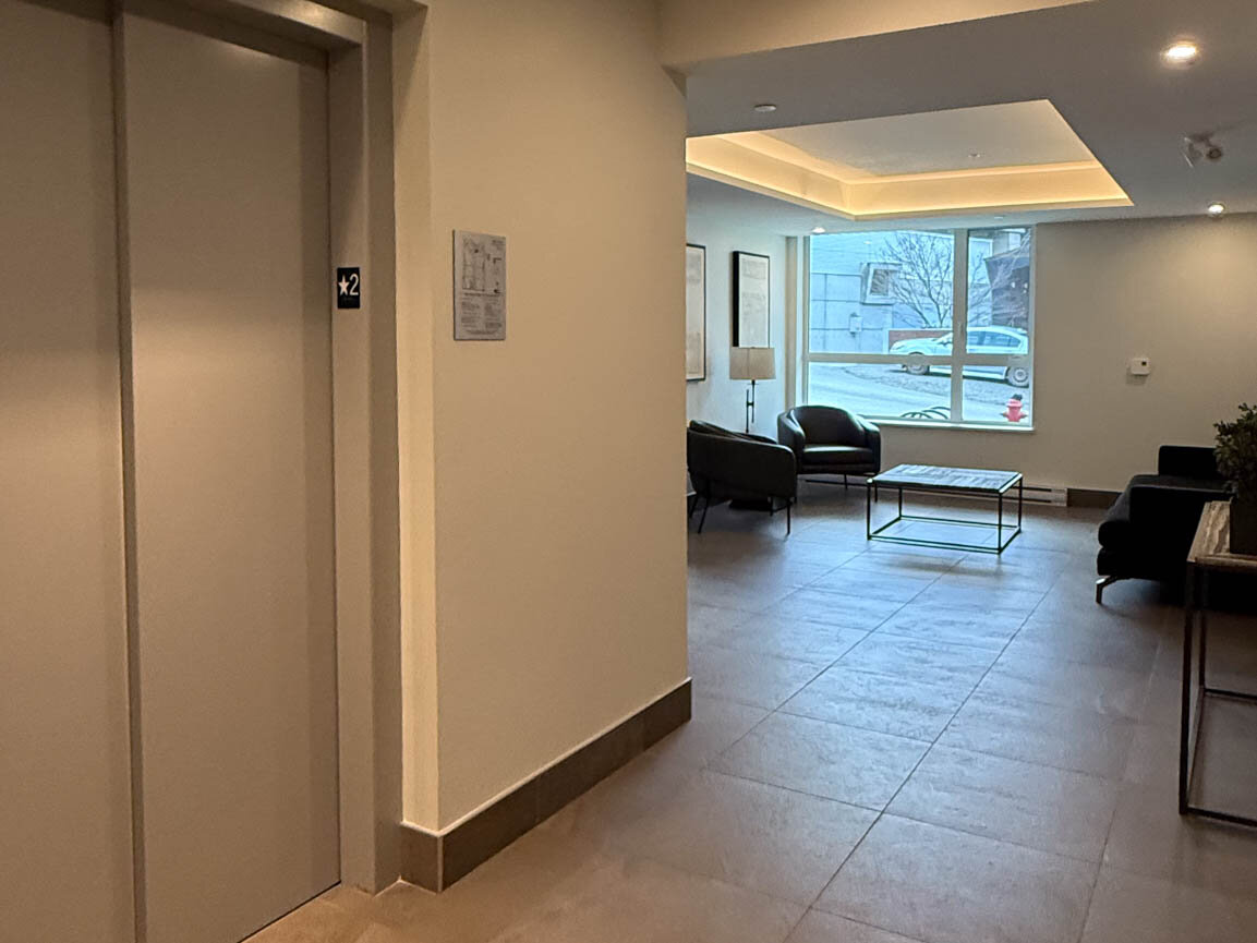 Lobby lounge with dark leather armchairs, glass coffee table, and adjacent elevator. - Hendry Place