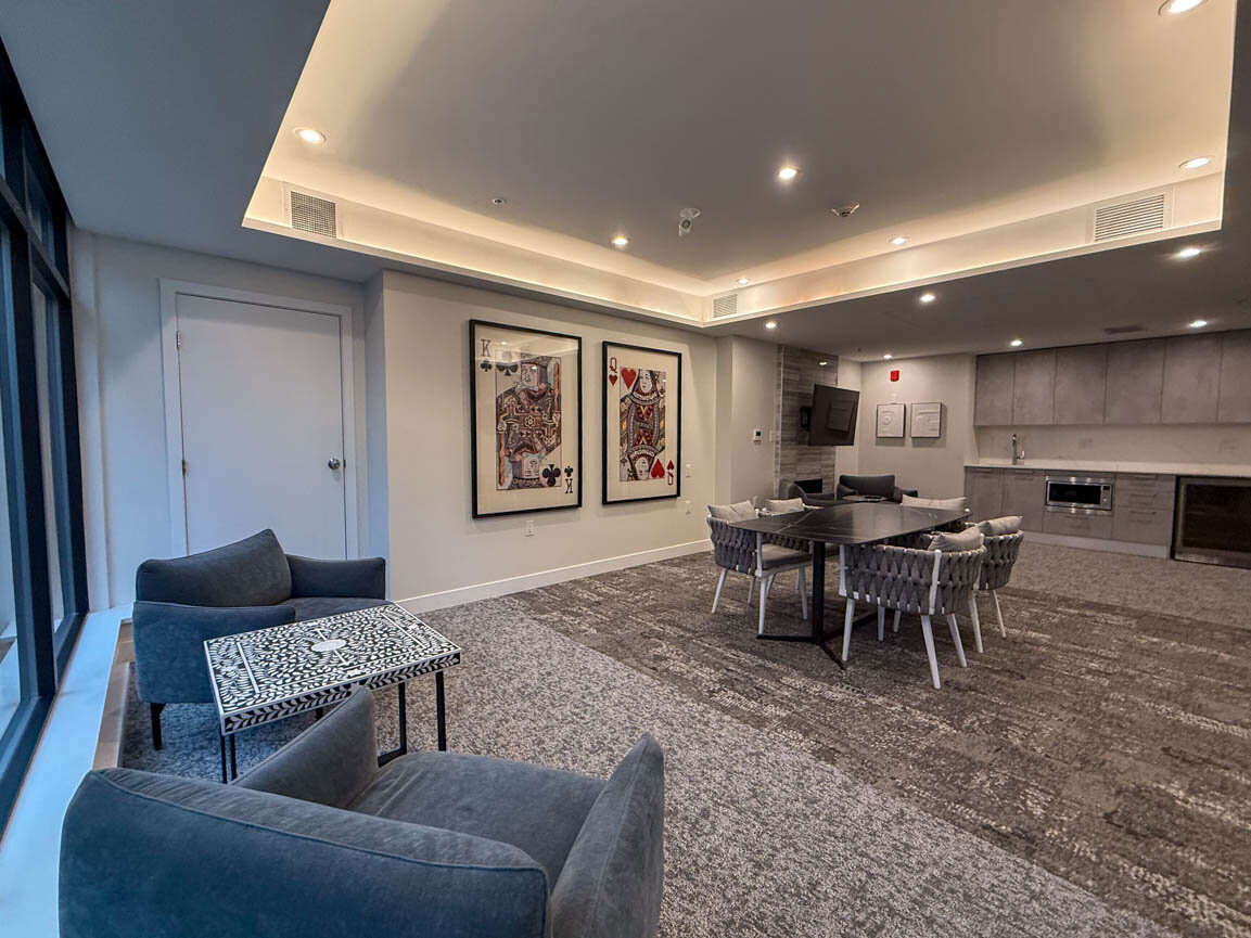 Communal lounge with a dining table, woven chairs, built-in kitchen, and framed playing-card wall art. - Hendry Place