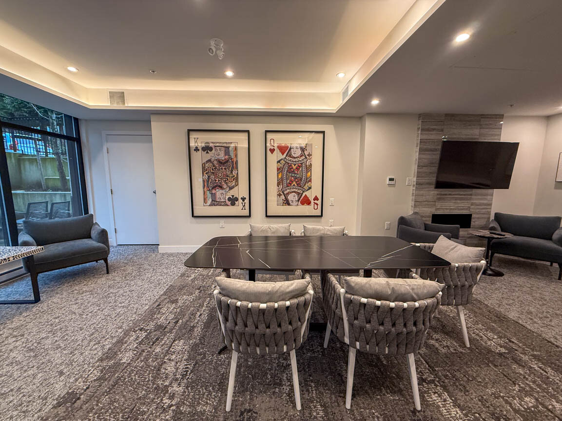 Common room featuring a dark marble dining table, woven accent chairs, and framed playing-card artwork. - Hendry Place