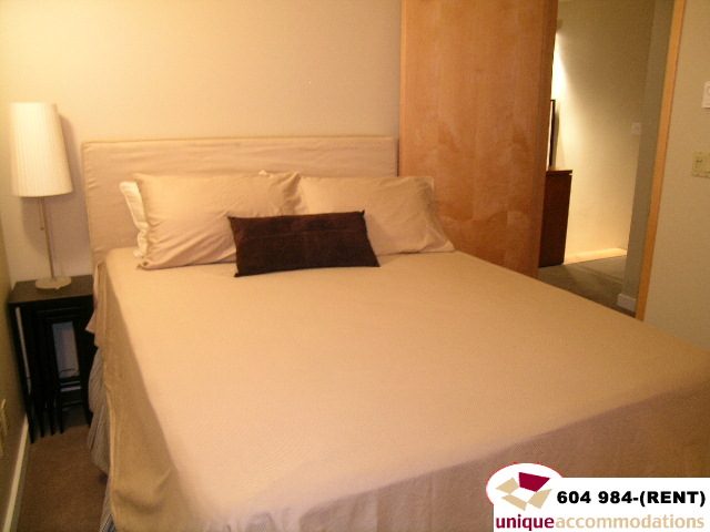 Furnished bedroom with white bedding and wooden headboard, clean and inviting. - 700 - 1888 York Ave, Vancouver West Side