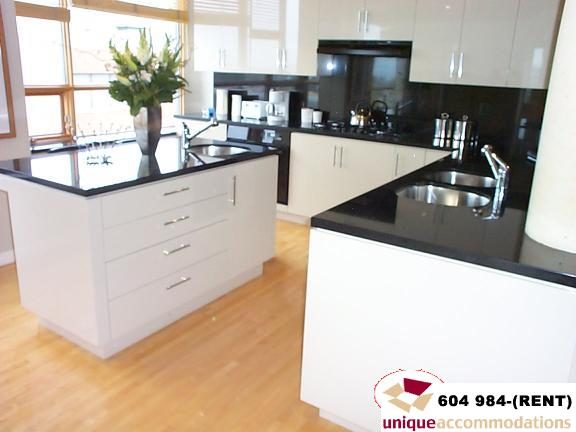 Bright kitchen with white cabinetry, black countertops, and hardwood floors. - 700 - 1888 York Ave, Vancouver West Side