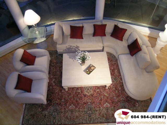 Furnished living room with white sectional sofa, red throw pillows, and patterned rug. - 700 - 1888 York Ave, Vancouver West Side