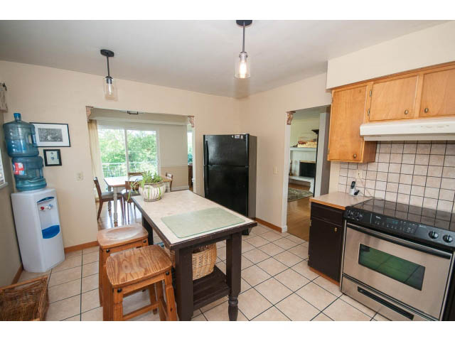 Bright kitchen with tiled floors, wooden cabinets, and a black refrigerator, leading to a dining area with a window view.
