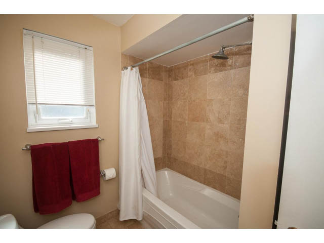 Bathroom with beige tiles, white fixtures, and red towels. - 1007 Shavington (Upper), North Vancouver