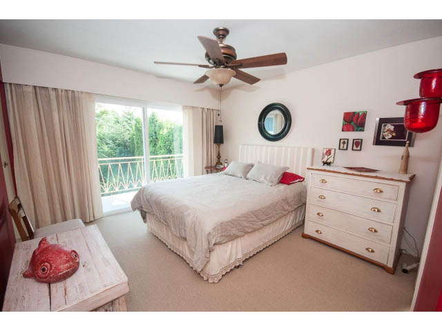 Bright bedroom with white furniture, red accents, and a view of greenery outside. - 1007 Shavington (Upper), North Vancouver