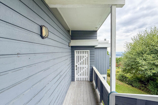 Covered balcony with weathered grey wood plank flooring and a white slatted door opening to lush greenery. - 1350 Crestwell Road, West Vancouver