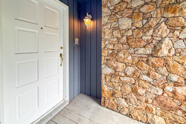 Front entryway with a white paneled door, dark blue wood siding, and a rustic stacked stone wall. - 1350 Crestwell Road, West Vancouver