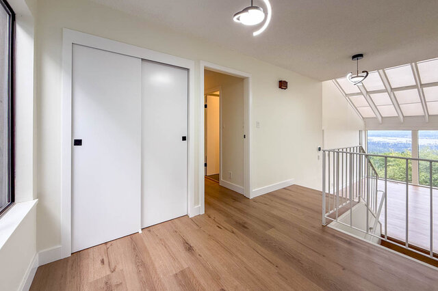 Upper landing with light wood floors, white sliding closet doors, and a railing overlooking a skylit lower level.