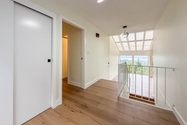 Bright upper hallway with hardwood floors, a white railing, and a skylight above. - 1350 Crestwell Road, West Vancouver