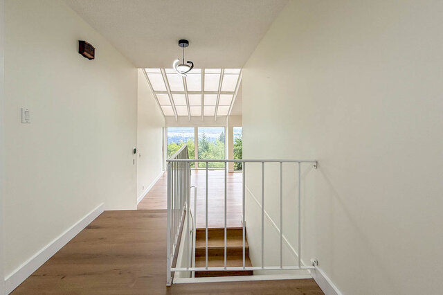 Bright hallway landing with hardwood floors, a white railing, and a treetop view through large windows. - 1350 Crestwell Road, West Vancouver