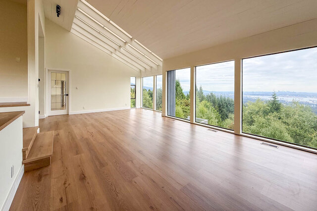 Spacious living room with hardwood floors and floor-to-ceiling windows framing a distant city and water view. - 1350 Crestwell Road, West Vancouver