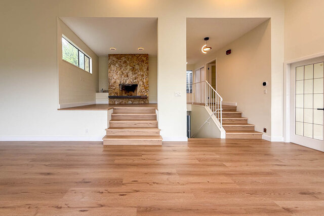 Spacious living room with light hardwood floors, a natural stone fireplace, and a white-railed staircase. - 1350 Crestwell Road, West Vancouver