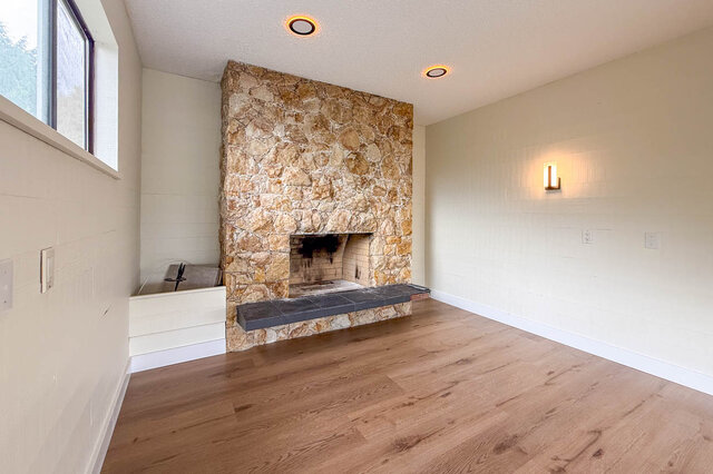 Spacious living room with a natural stone fireplace and light hardwood floors. - 1350 Crestwell Road, West Vancouver