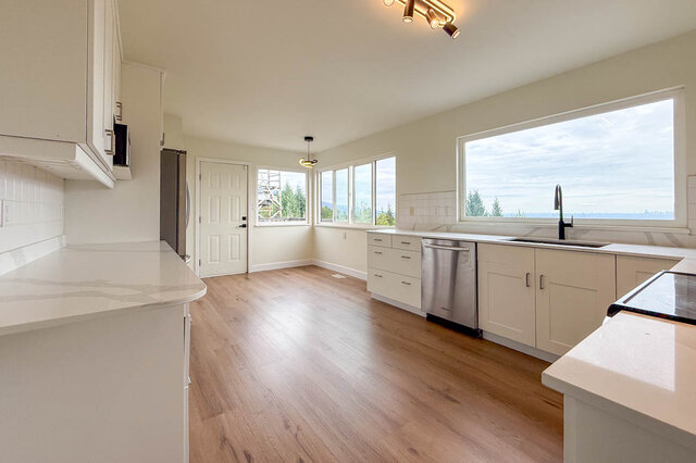 Bright kitchen with white cabinets, quartz countertops, and hardwood floors overlooking the water. - 1350 Crestwell Road, West Vancouver