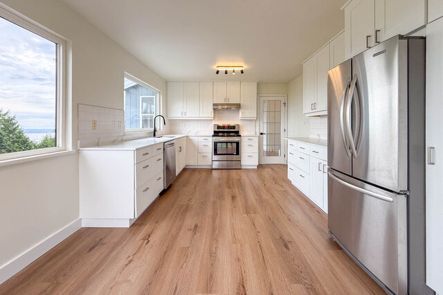 Bright kitchen with white cabinets, stainless steel appliances, hardwood floors, and a water view. - 1350 Crestwell Road, West Vancouver