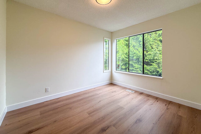 Empty bedroom with hardwood floors and large windows framing a lush green tree view. - 1350 Crestwell Road, West Vancouver