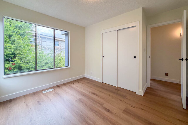 Bright bedroom with light hardwood floors, a large window framing green trees, and white sliding closet doors. - 1350 Crestwell Road, West Vancouver