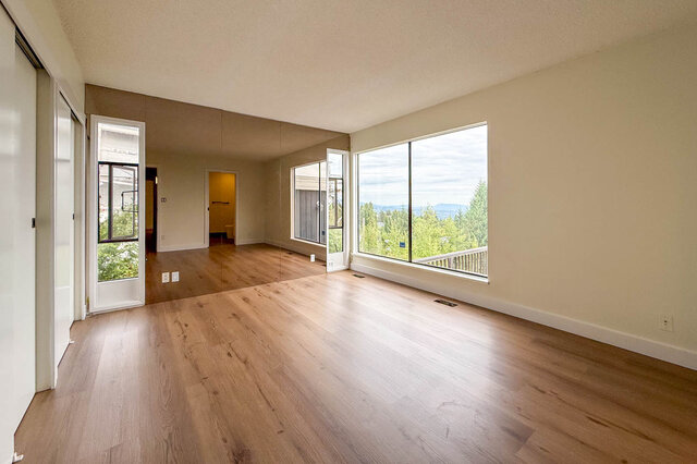 Spacious living room with hardwood floors and large windows framing a tree and water view. - 1350 Crestwell Road, West Vancouver