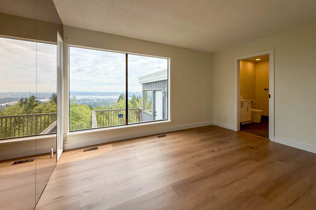 Bright bedroom with hardwood floors and large windows overlooking a tree-lined city view. - 1350 Crestwell Road, West Vancouver