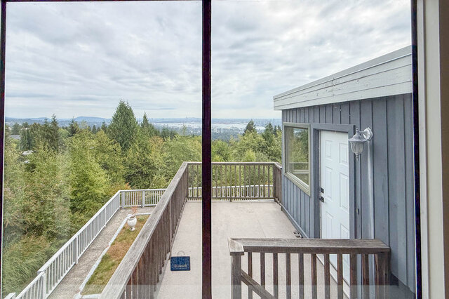 Elevated balcony with wooden railings offering a panoramic view of trees and distant city skyline. - 1350 Crestwell Road, West Vancouver