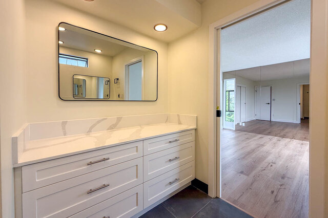 Modern bathroom vanity with white marble-look countertop, white drawers, and a large black-framed mirror. - 1350 Crestwell Road, West Vancouver