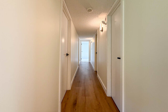 Long hallway with hardwood floors and white doors on both sides, lit by wall sconces. - 1350 Crestwell Road, West Vancouver