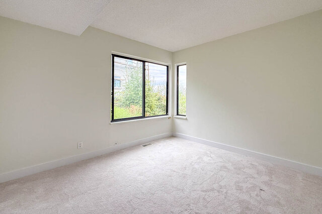 Empty bedroom with light carpet and black-framed windows overlooking greenery. - 1350 Crestwell Road, West Vancouver