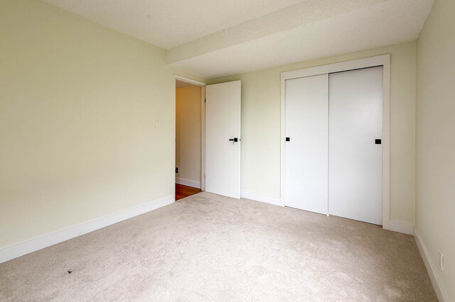 Empty carpeted bedroom with white sliding closet doors and an open interior doorway. - 1350 Crestwell Road, West Vancouver