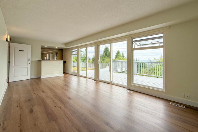 Spacious living room with light hardwood floors and a wall of windows opening to a deck with a scenic view. - 1350 Crestwell Road, West Vancouver