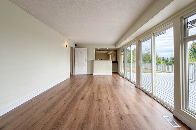 Spacious living room with hardwood floors and a wall of windows opening to a deck with a tree-lined view. - 1350 Crestwell Road, West Vancouver