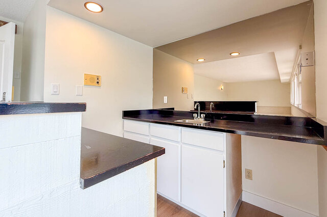 Kitchen with dark countertops, white cabinetry, and a large wall mirror reflecting recessed lighting. - 1350 Crestwell Road, West Vancouver