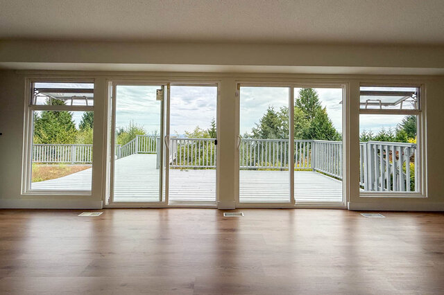 Spacious living room with hardwood floors and sliding glass doors opening to a white deck surrounded by trees. - 1350 Crestwell Road, West Vancouver