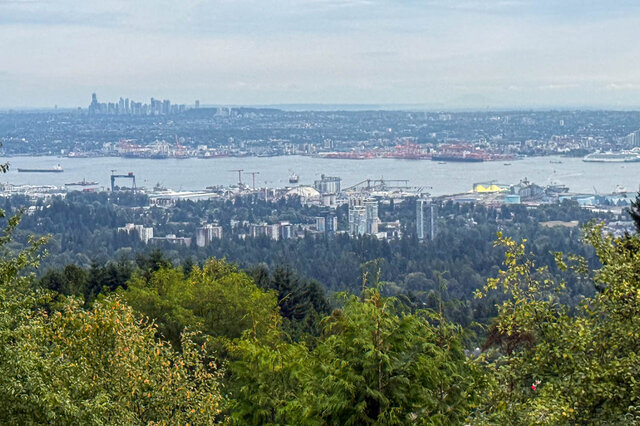 Elevated view over lush green treetops toward a hazy city skyline and waterfront across the water. - 1350 Crestwell Road, West Vancouver