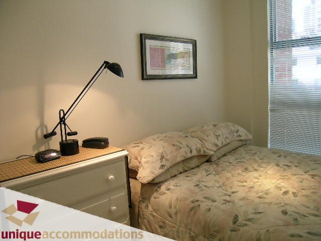 Bright bedroom with floral bedding and a desk lamp, natural light from window. - 509 - 939  Homer Street, Vancouver Downtown