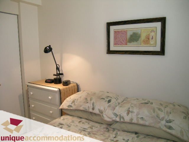 Bright bedroom with floral bedding and a desk lamp, framed artwork on the wall. - 509 - 939  Homer Street, Vancouver Downtown