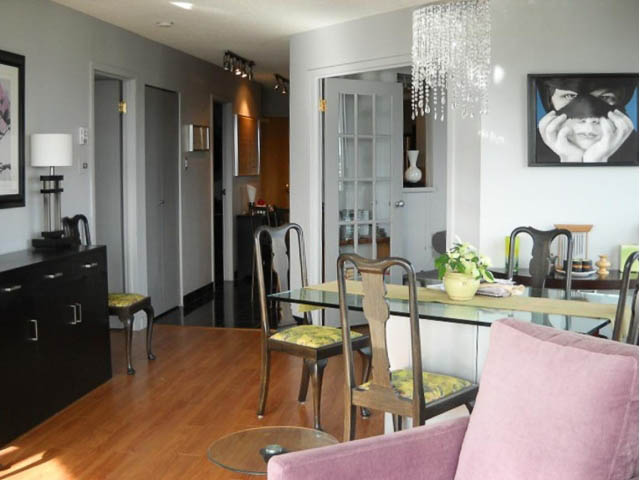 Furnished living room with hardwood floors and a chandelier, leading to a dining area with a glass table and chairs.