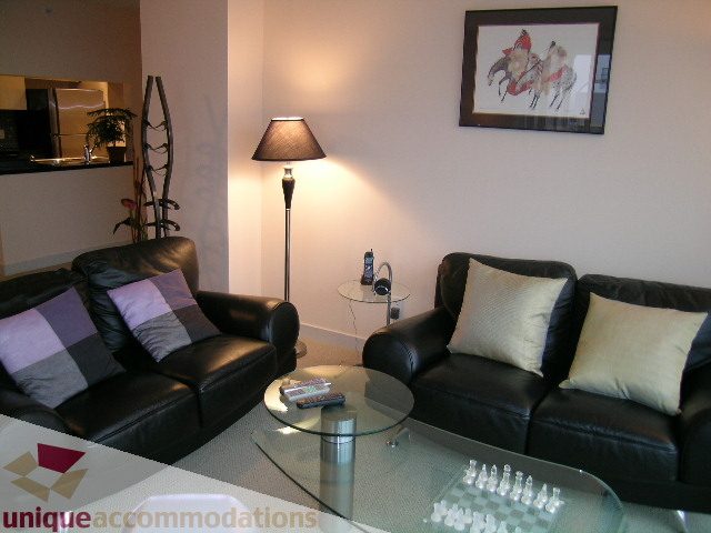 Furnished living room with black leather couches, glass coffee table, and floor lamp. - 3101 - 1408 Strathmore Mews, Vancouver Downtown