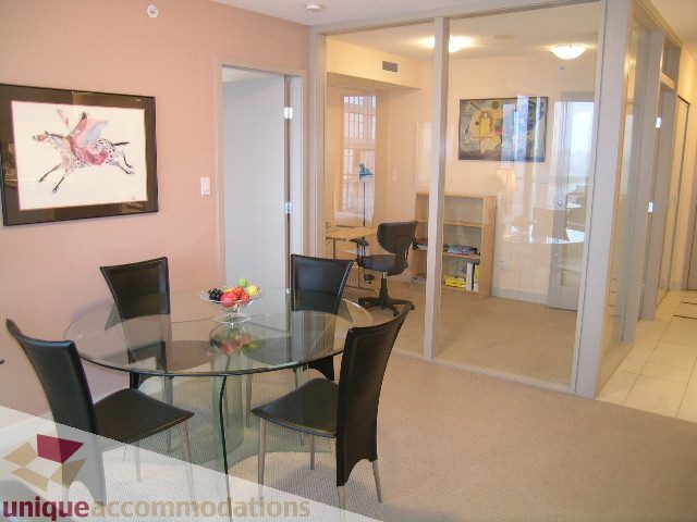 Furnished dining area with glass table and black chairs, leading to a living room with sliding glass doors.
