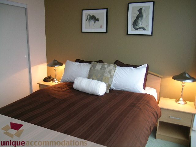 Furnished bedroom with brown bedding, two lamps, and wall art. - 3101 - 1408 Strathmore Mews, Vancouver Downtown