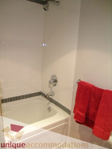 Furnished bathroom with white tiles, red towels, and a corner shower. - 3101 - 1408 Strathmore Mews, Vancouver Downtown