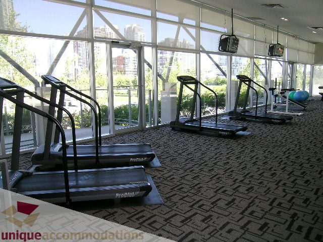 Bright fitness room with treadmills, city view, and carpeted floor. - 3101 - 1408 Strathmore Mews, Vancouver Downtown