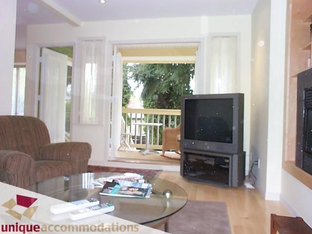 Living room with hardwood floors and a glass coffee table, featuring a flat-screen TV and large windows. - 2750 Waterloo Street, Vancouver West Side