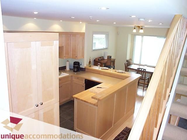 Bright kitchen with light wood cabinets and a breakfast bar, leading to a dining area with a large window. - 2750 Waterloo Street, Vancouver West Side