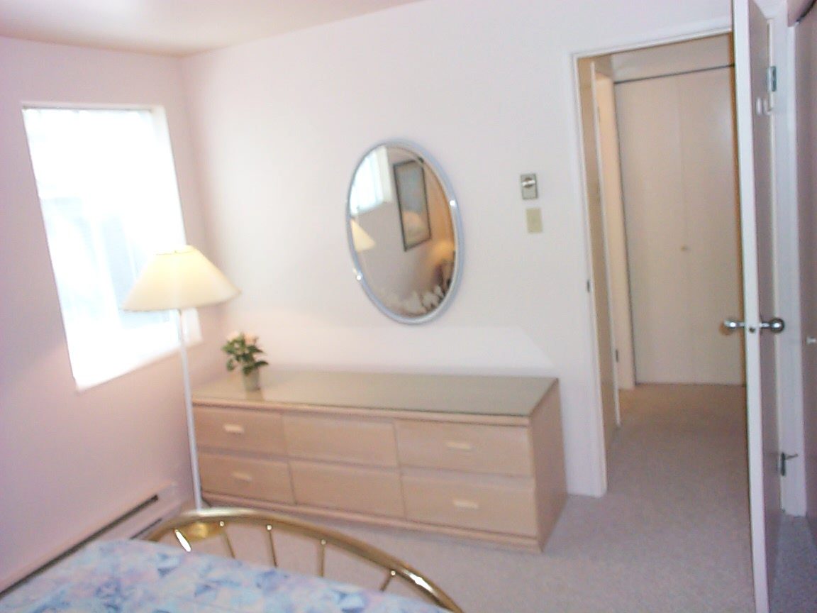 Bright bedroom with white walls, large oval mirror, and a dresser with a lamp. - 832 West 7th Avenue, Vancouver West Side