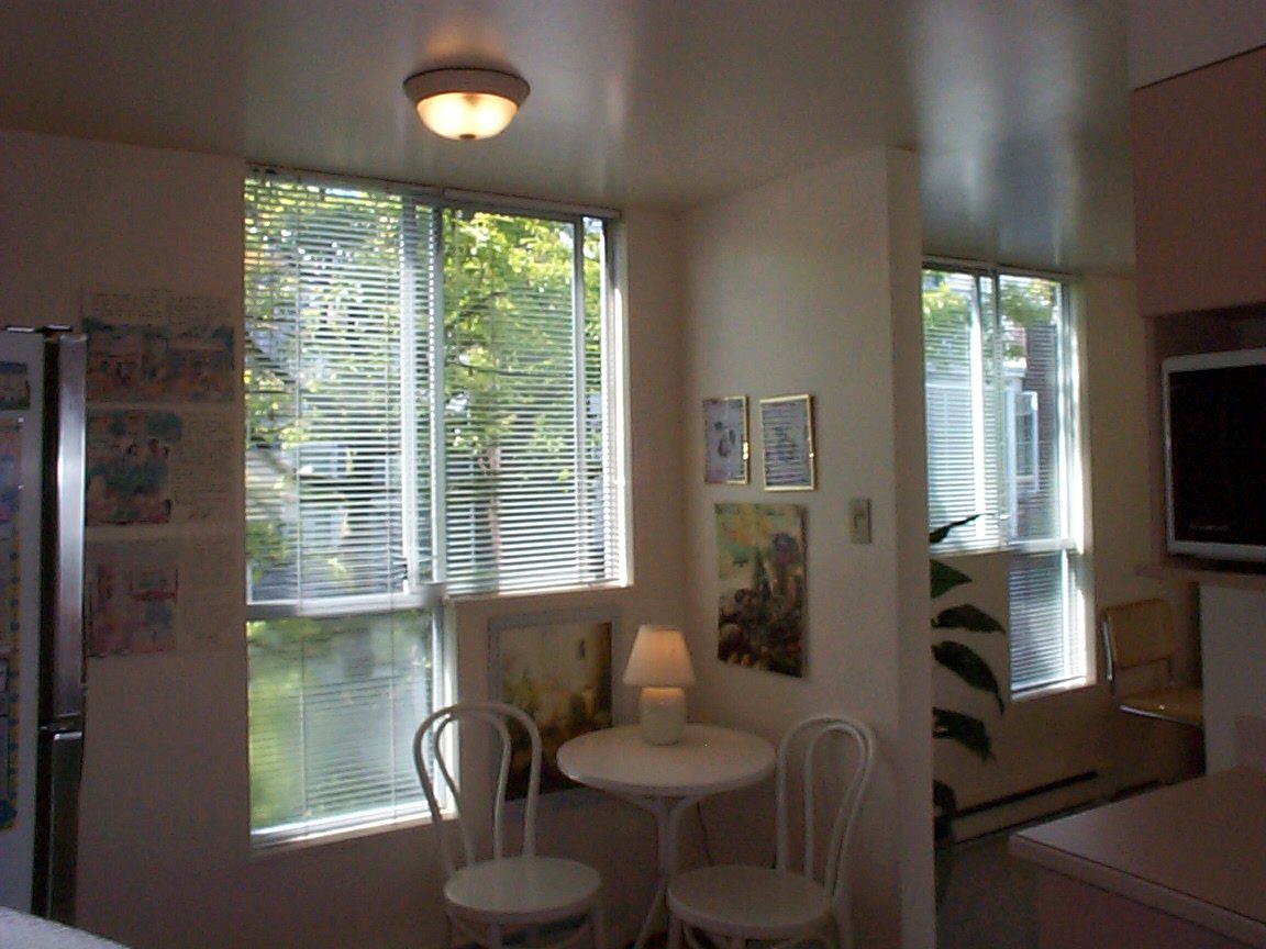 Bright dining area with white chairs, small table, and wall art, natural light from large windows. - 832 West 7th Avenue, Vancouver West Side