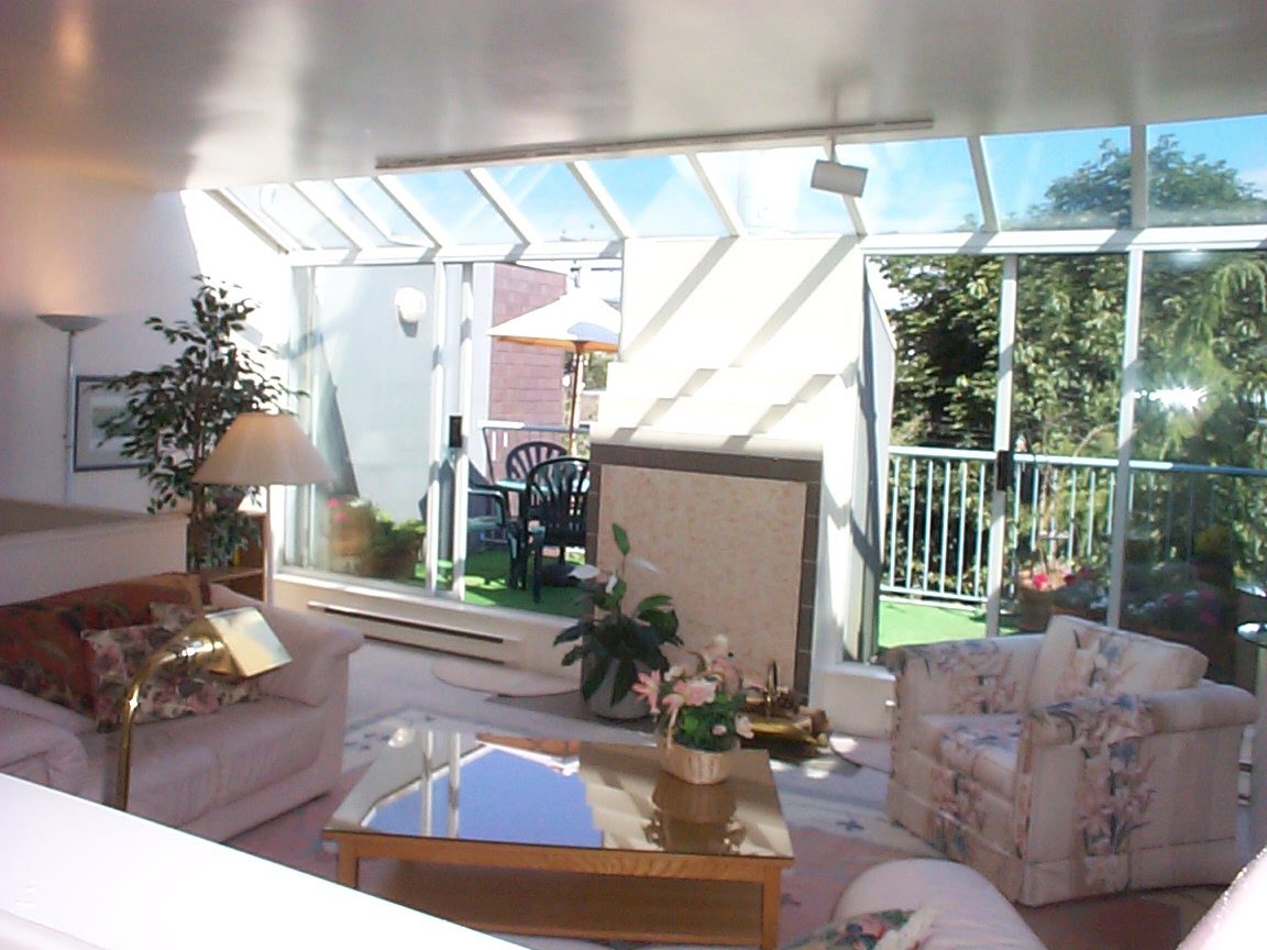 Bright sunroom with large windows, outdoor seating, and lush greenery visible outside. - 832 West 7th Avenue, Vancouver West Side
